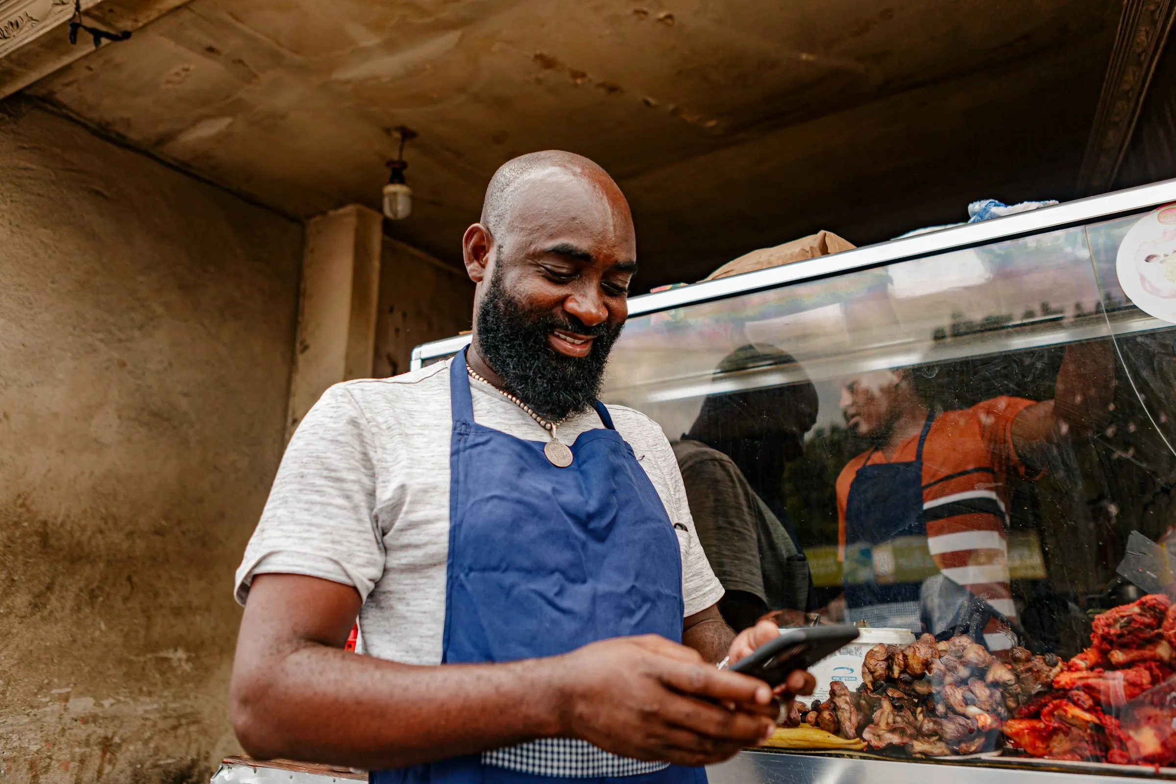 A shop owner at the counter of his spaza shop, checking stock on his phone.