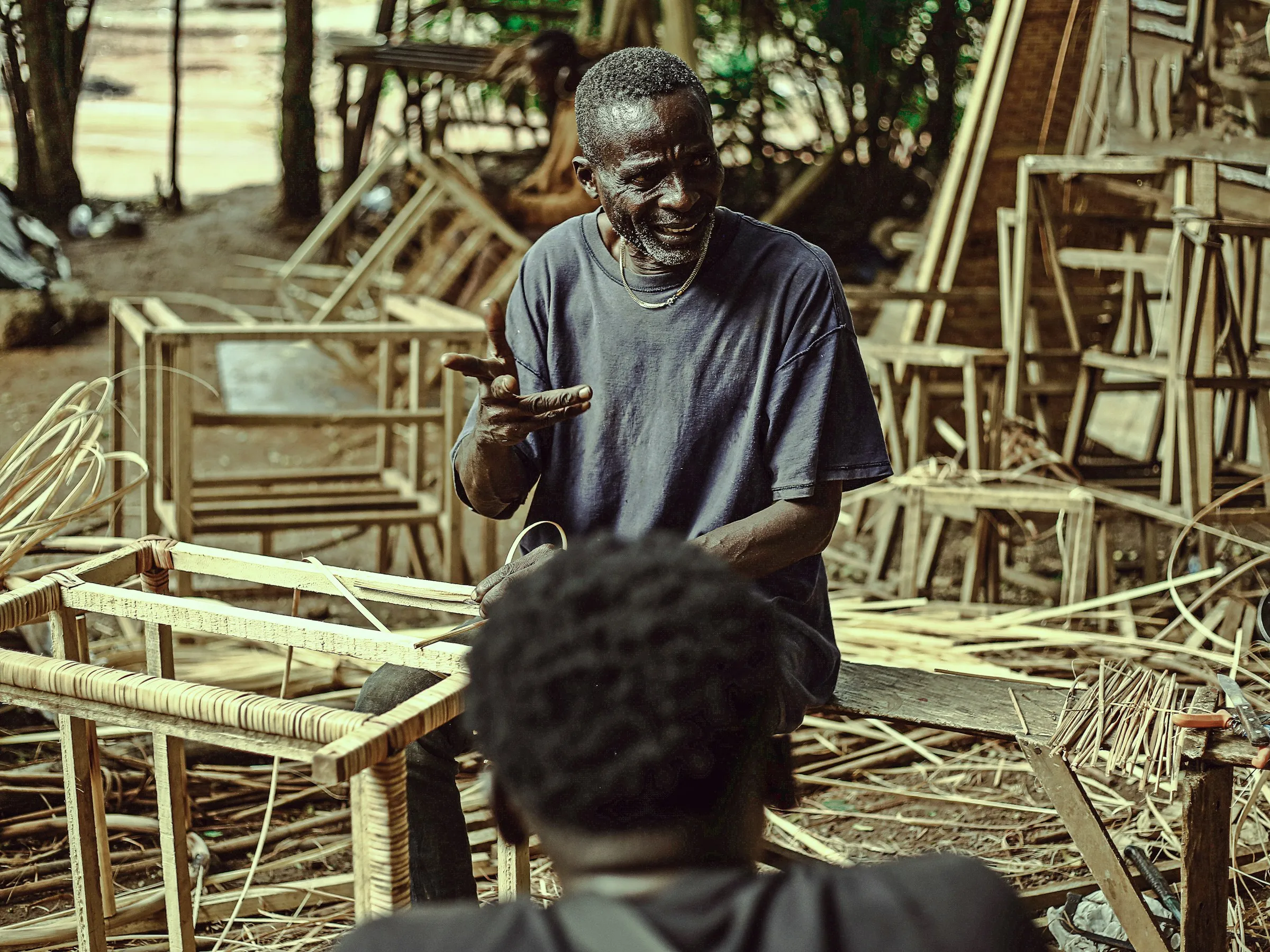 A furniture maker in his workshop explaining his work to a colleague.